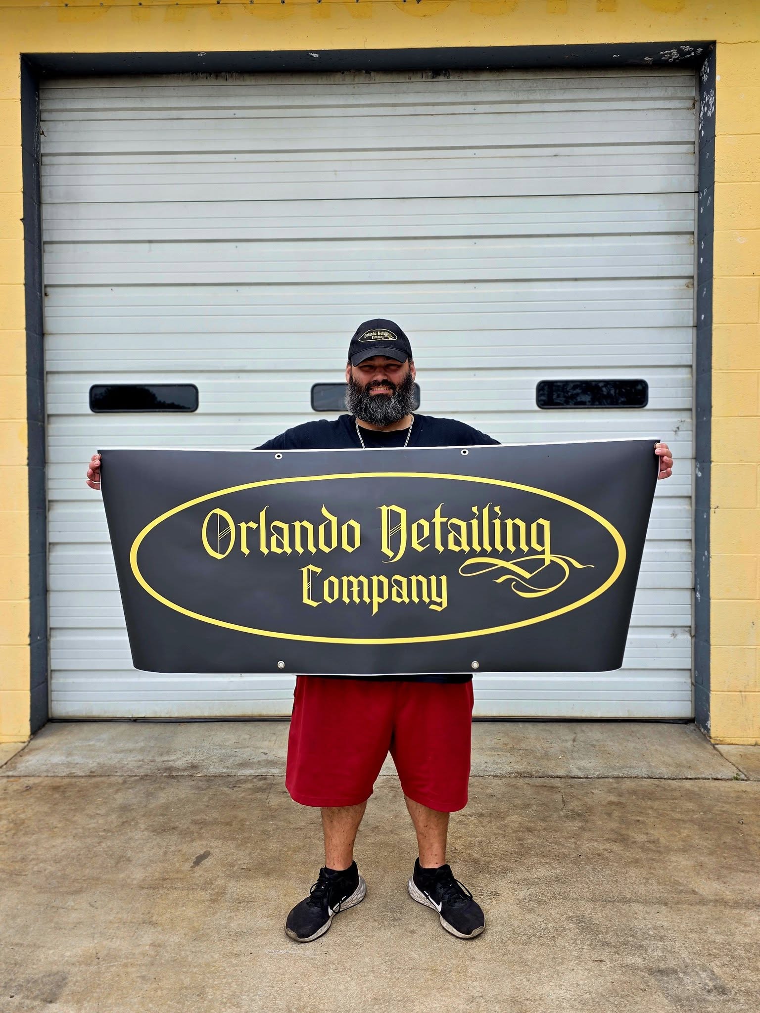 The owner of Orlando Detailing Company holding the company sign outside the McMinnville shop